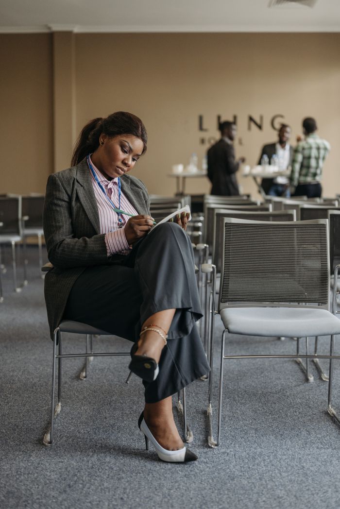 Businesswoman in formal attire writing notes during a conference session.